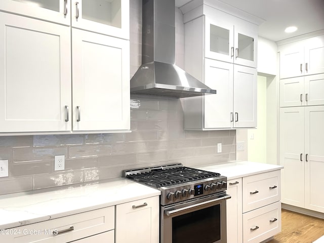 kitchen with white cabinetry, stainless steel range with gas stovetop, light stone counters, wall chimney exhaust hood, and light wood-type flooring