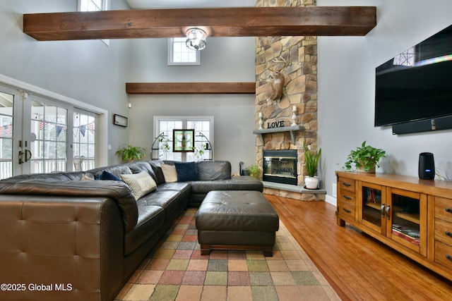 living room with french doors, a towering ceiling, light wood-style floors, a stone fireplace, and beamed ceiling