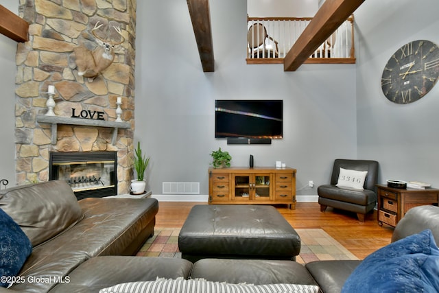 living room featuring a stone fireplace, wood finished floors, visible vents, and baseboards