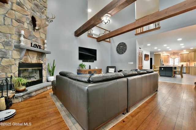 living area with light wood-style floors, recessed lighting, beam ceiling, and a stone fireplace