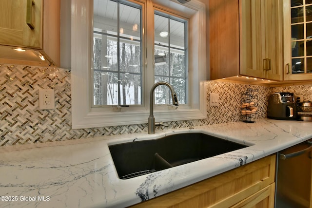 kitchen featuring a sink, stainless steel dishwasher, light stone countertops, tasteful backsplash, and glass insert cabinets