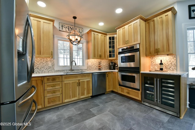 kitchen with decorative light fixtures, stainless steel appliances, light brown cabinets, a sink, and beverage cooler