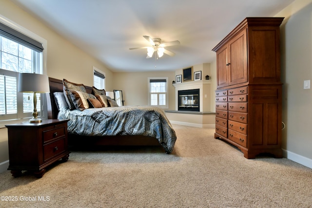 bedroom featuring baseboards, a glass covered fireplace, and light colored carpet