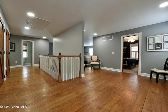 corridor featuring visible vents, hardwood / wood-style flooring, an upstairs landing, and baseboards