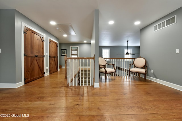 corridor featuring baseboards, visible vents, light wood finished floors, and an upstairs landing