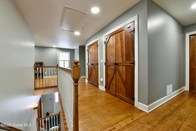 hall with attic access, baseboards, wood finished floors, and an upstairs landing