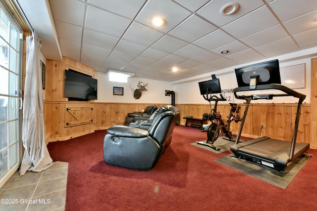 exercise room featuring wooden walls, a drop ceiling, a wealth of natural light, and wainscoting