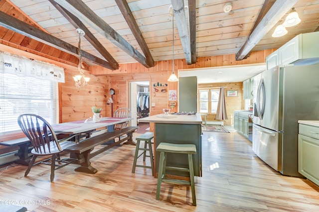 kitchen with stainless steel fridge, hanging light fixtures, a kitchen bar, wooden walls, and a kitchen island