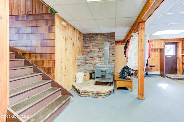 basement with wooden walls, a wood stove, and a paneled ceiling