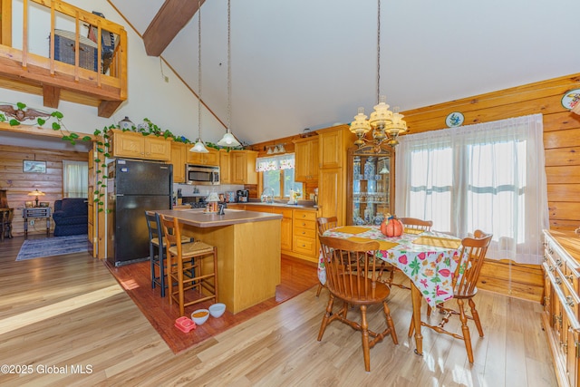 kitchen featuring light hardwood / wood-style flooring, a kitchen island with sink, beam ceiling, high vaulted ceiling, and black fridge