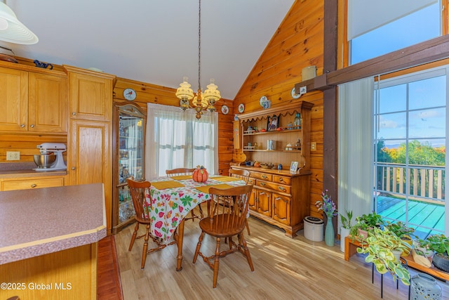 dining space featuring lofted ceiling, a notable chandelier, wooden walls, and light hardwood / wood-style flooring