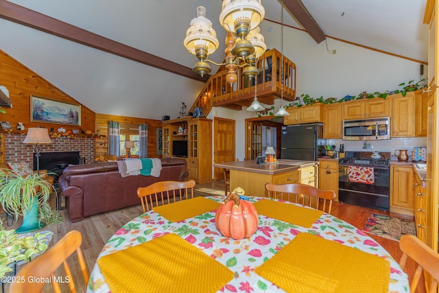 dining area with wood walls, beamed ceiling, a chandelier, a brick fireplace, and light hardwood / wood-style flooring