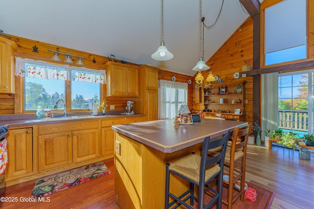 kitchen with sink, a breakfast bar area, wooden walls, a kitchen island, and light wood-type flooring