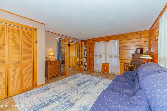 bedroom with wood walls, french doors, a closet, crown molding, and light hardwood / wood-style flooring