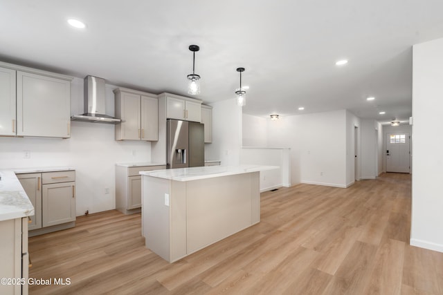 kitchen with gray cabinets, a kitchen island, pendant lighting, stainless steel fridge, and wall chimney exhaust hood