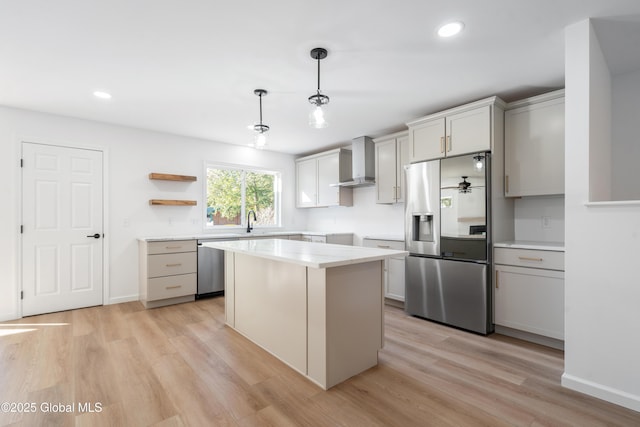 kitchen featuring wall chimney exhaust hood, light hardwood / wood-style flooring, a kitchen island, pendant lighting, and stainless steel appliances