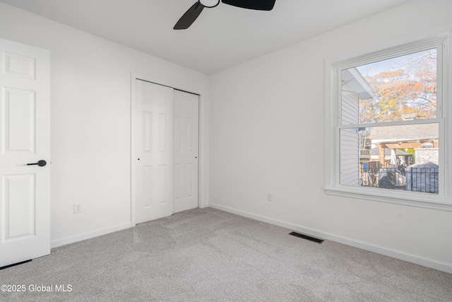 unfurnished bedroom featuring multiple windows, carpet flooring, ceiling fan, and a closet