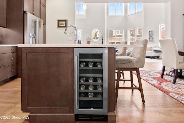 bar with light wood-type flooring, wine cooler, a towering ceiling, and high end refrigerator