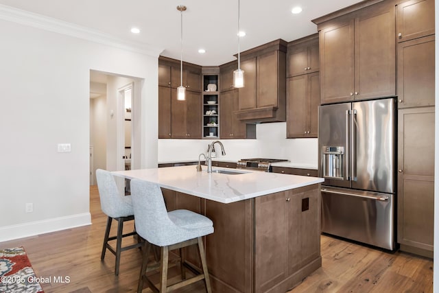 kitchen with high quality appliances, hanging light fixtures, a kitchen island with sink, open shelves, and a sink