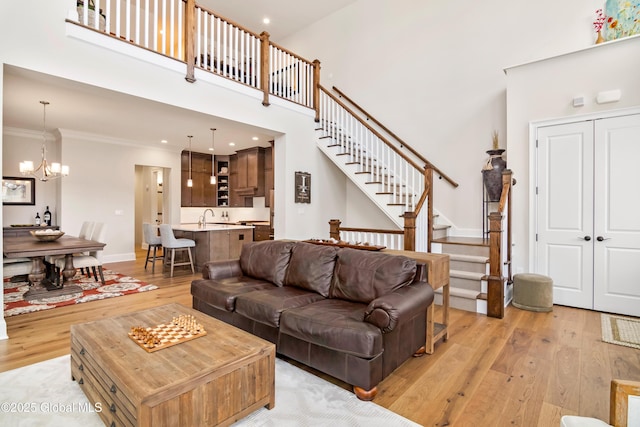 living area with crown molding, light wood-style flooring, a high ceiling, and stairs