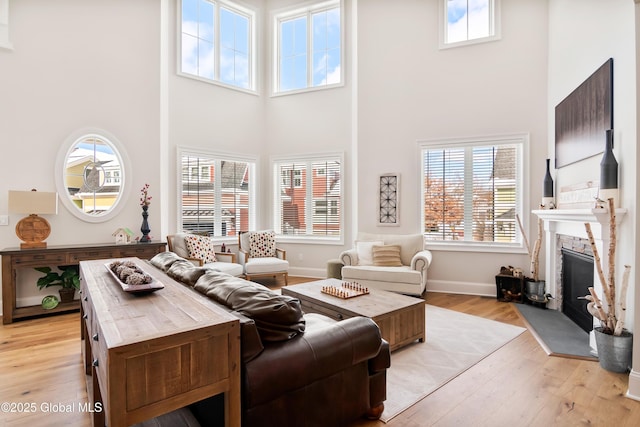 living area featuring a towering ceiling, light wood-style floors, a fireplace, and baseboards