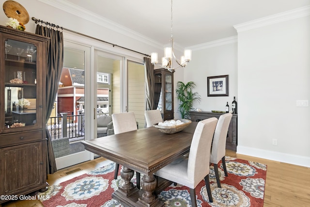 dining room with a notable chandelier, visible vents, baseboards, ornamental molding, and light wood finished floors