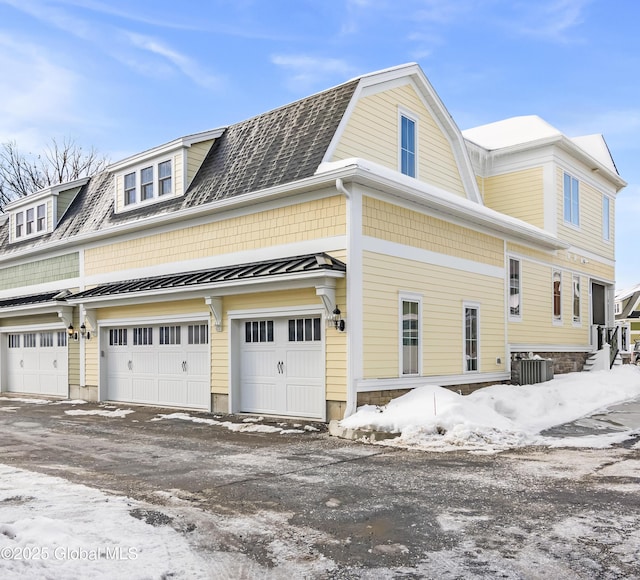 view of snow covered exterior with roof with shingles, a standing seam roof, a gambrel roof, central air condition unit, and metal roof