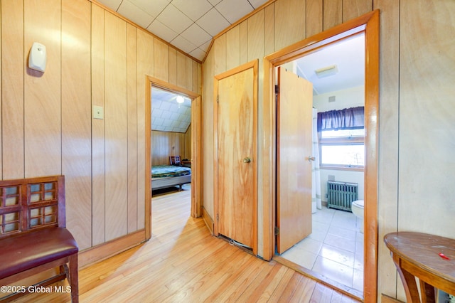 corridor featuring lofted ceiling, radiator, light wood-type flooring, and wood walls