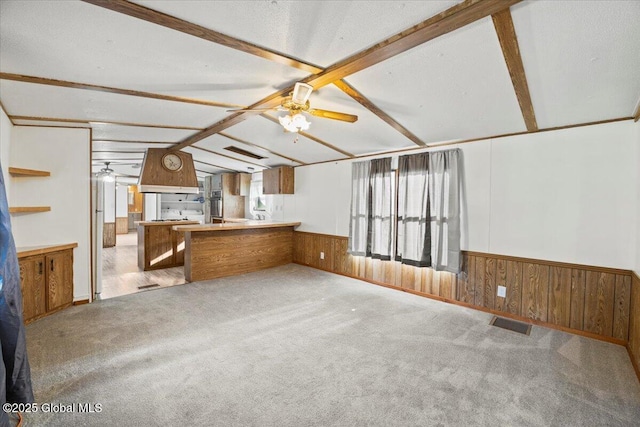 kitchen featuring lofted ceiling with beams, light carpet, wooden walls, kitchen peninsula, and ceiling fan