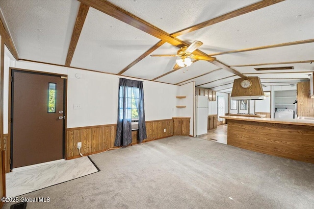 unfurnished living room featuring wooden walls, washer and clothes dryer, a textured ceiling, and vaulted ceiling with beams