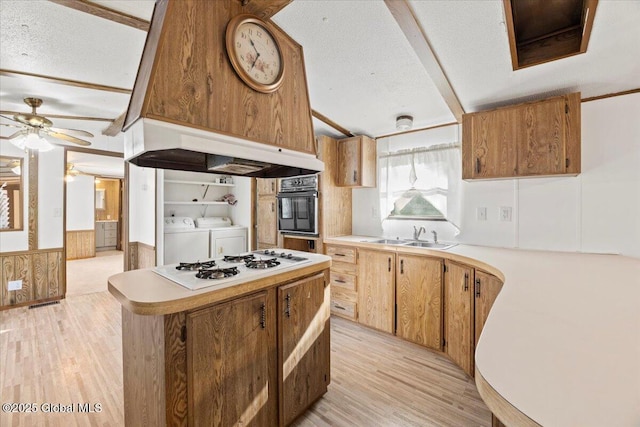 kitchen with premium range hood, sink, light wood-type flooring, washer and clothes dryer, and a textured ceiling