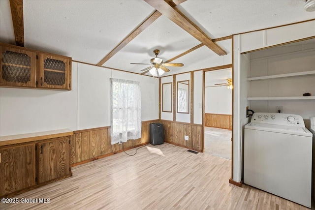 clothes washing area featuring wood walls, washer / dryer, light wood-type flooring, ceiling fan, and a textured ceiling