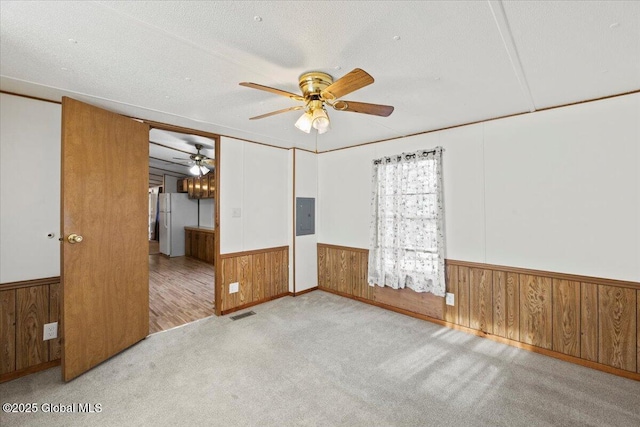 unfurnished bedroom with electric panel, white refrigerator, a textured ceiling, light carpet, and wood walls