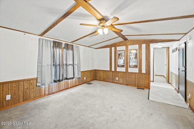 carpeted empty room featuring a textured ceiling, lofted ceiling with beams, ceiling fan, and wood walls