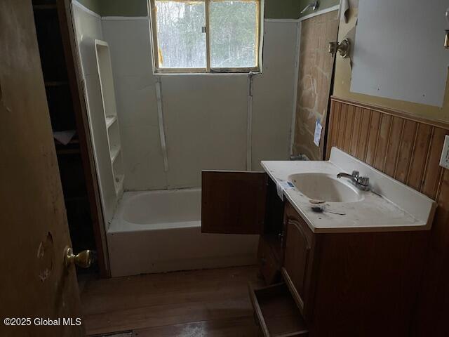 bathroom with hardwood / wood-style flooring, vanity, wooden walls, and shower / bathtub combination