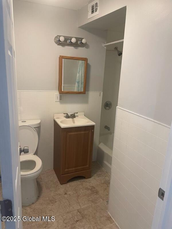 bathroom with tile walls, visible vents, toilet, vanity, and  shower combination