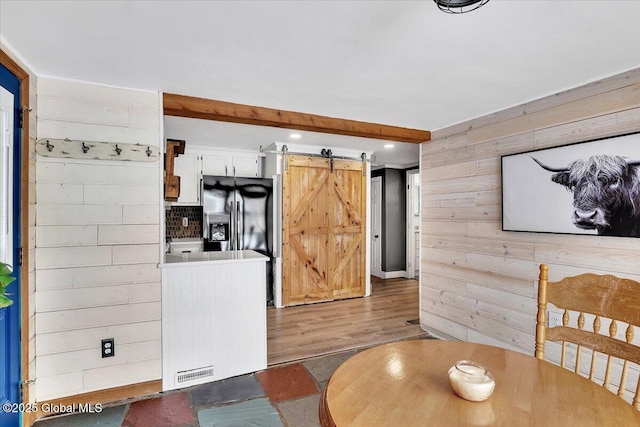 dining space with beam ceiling, wood-type flooring, a barn door, and wooden walls