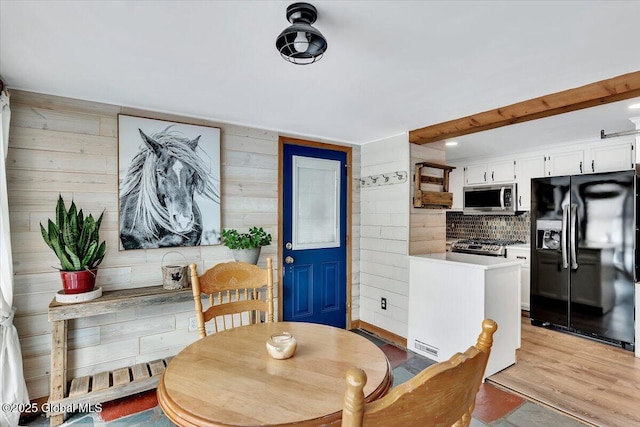 dining space with light hardwood / wood-style floors, beamed ceiling, and wood walls