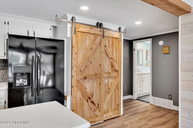 kitchen with white cabinets, crown molding, a barn door, black refrigerator with ice dispenser, and light hardwood / wood-style flooring