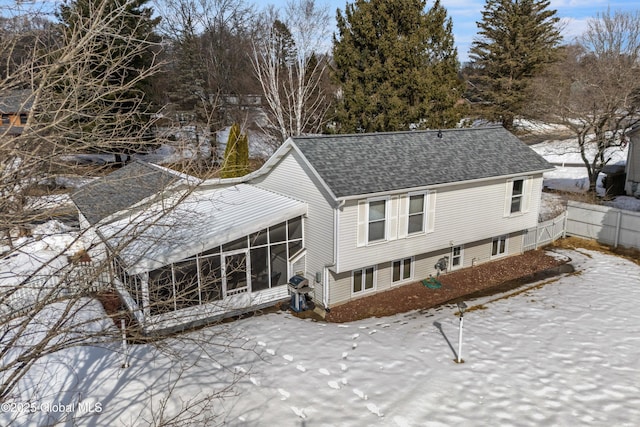 snow covered property featuring a sunroom and a shingled roof