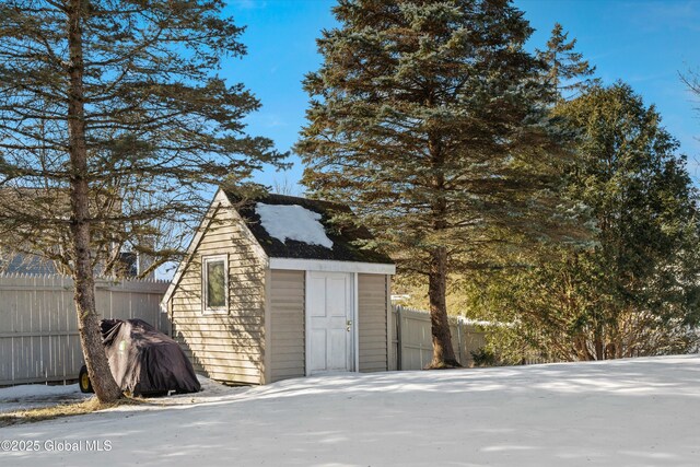 snow covered structure with an outdoor structure, a storage shed, and fence