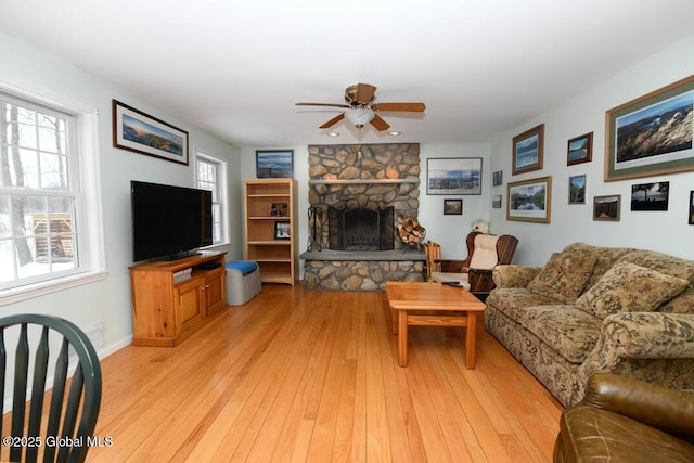 living room featuring a stone fireplace, light hardwood / wood-style floors, and ceiling fan