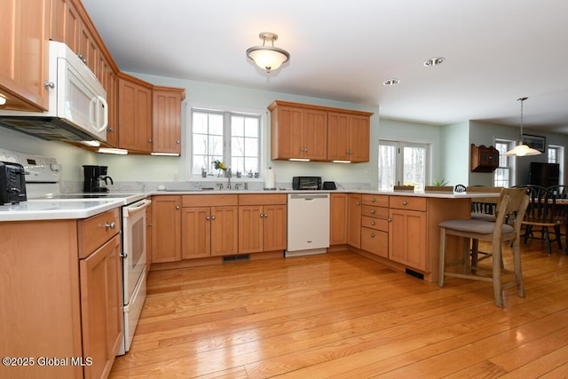 kitchen with a kitchen bar, light wood-type flooring, kitchen peninsula, pendant lighting, and white appliances