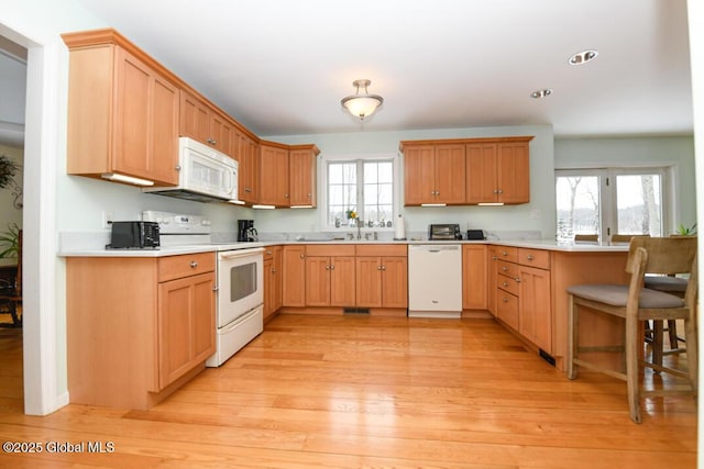 kitchen with a breakfast bar, sink, light hardwood / wood-style flooring, kitchen peninsula, and white appliances