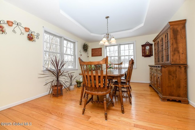 dining space featuring an inviting chandelier, a tray ceiling, and light hardwood / wood-style floors