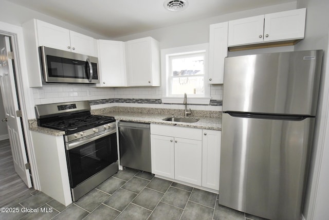 kitchen with sink, appliances with stainless steel finishes, white cabinets, light stone countertops, and backsplash