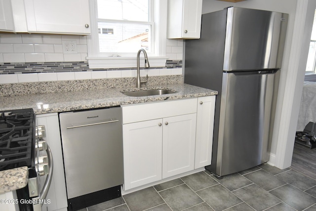 kitchen featuring stainless steel appliances, white cabinetry, light stone countertops, and sink