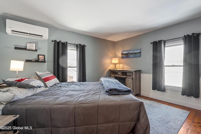 bedroom featuring an AC wall unit, wainscoting, and dark wood finished floors