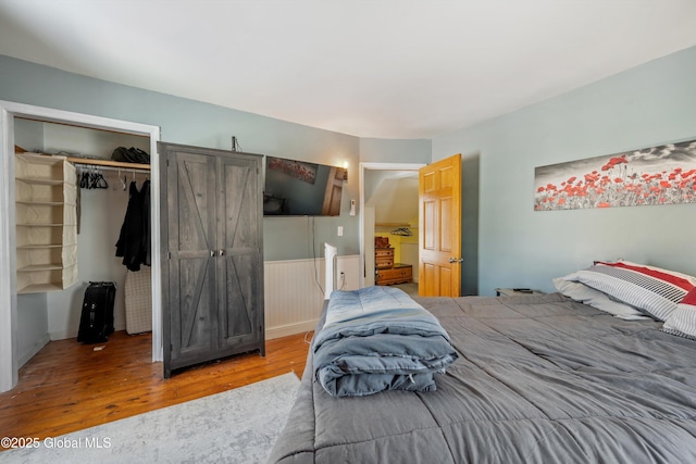 bedroom with a closet, wainscoting, and wood finished floors