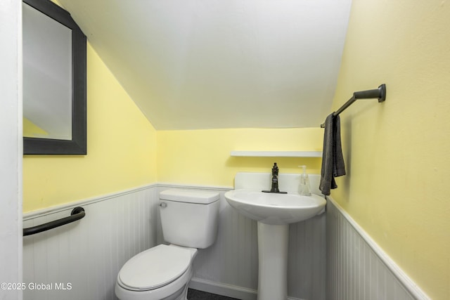 half bathroom with a wainscoted wall, vaulted ceiling, and toilet